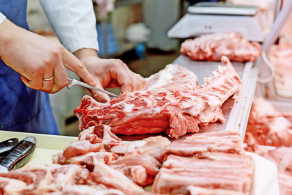 Cropped image of male butcher cutting raw meat with knife at counter shop